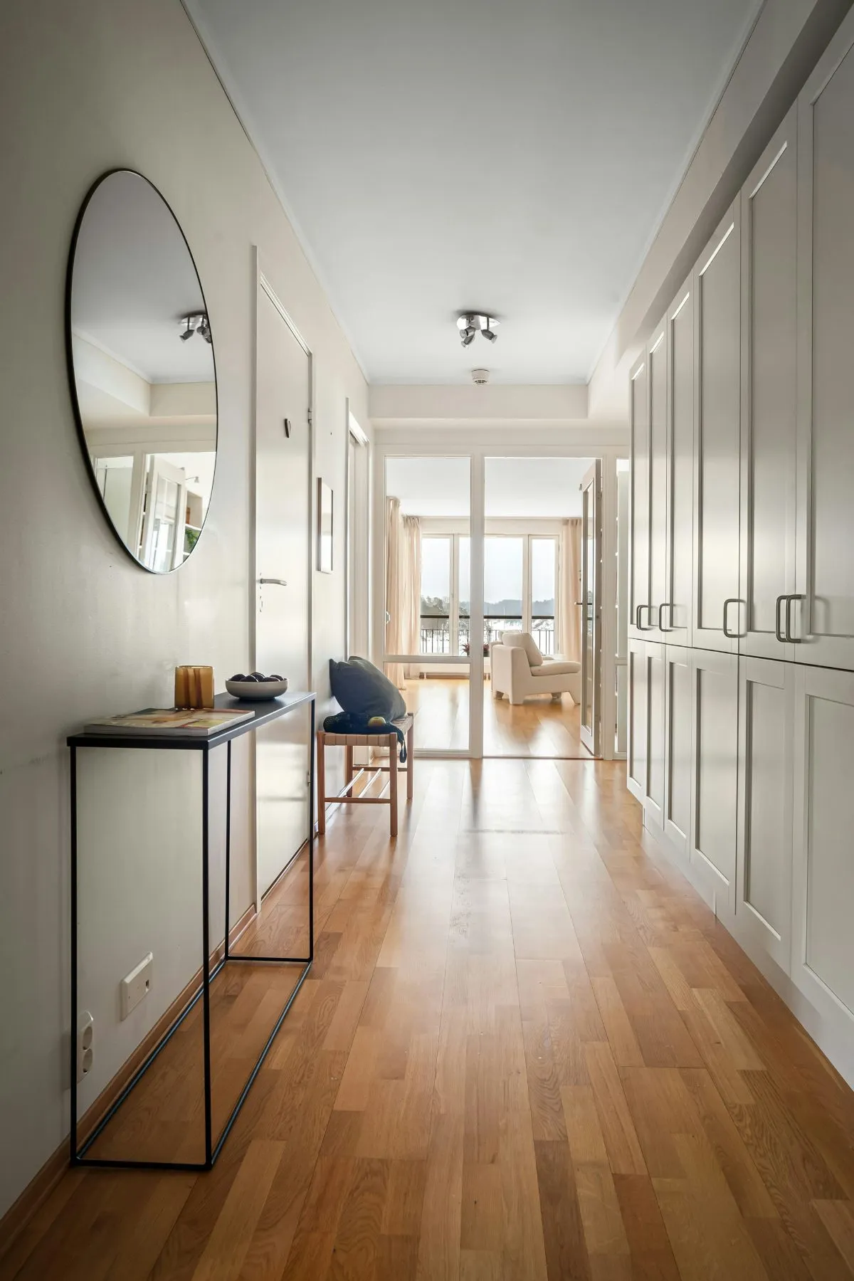 Warm oak-look laminate flooring running down a bright hallway toward a sunlit living room